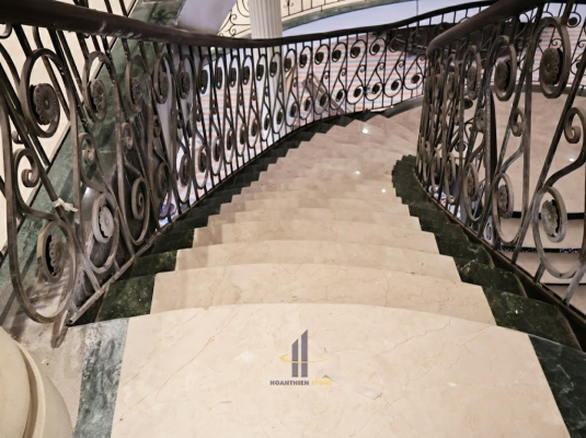 Thi công đá Marble màu kem cho cầu thang cong biệt thự tân cổ điển với lan can sắt nghệ thuật sang trọng.
